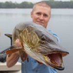 A man holding a fish in front of a body of water