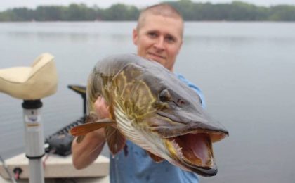 A man holding a fish in front of a body of water